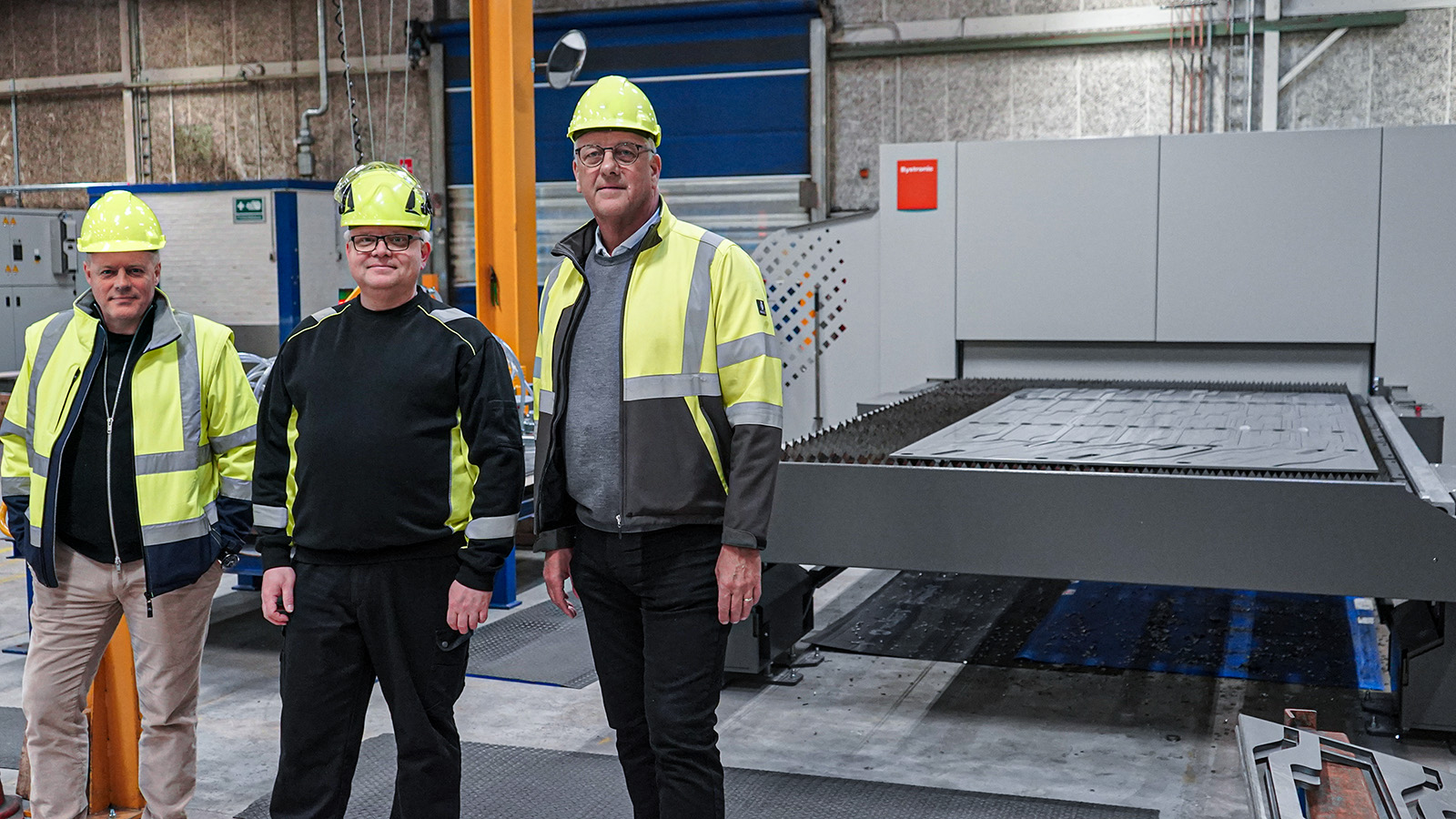 Lars, Jan and Hans standing by a fiber laser machine used in production at the Langeskov facility.